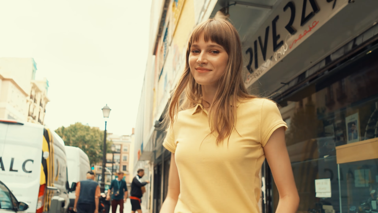 🟡 Persona portant un polo groc personalitzat, caminant per un carrer comercial de Barcelona.