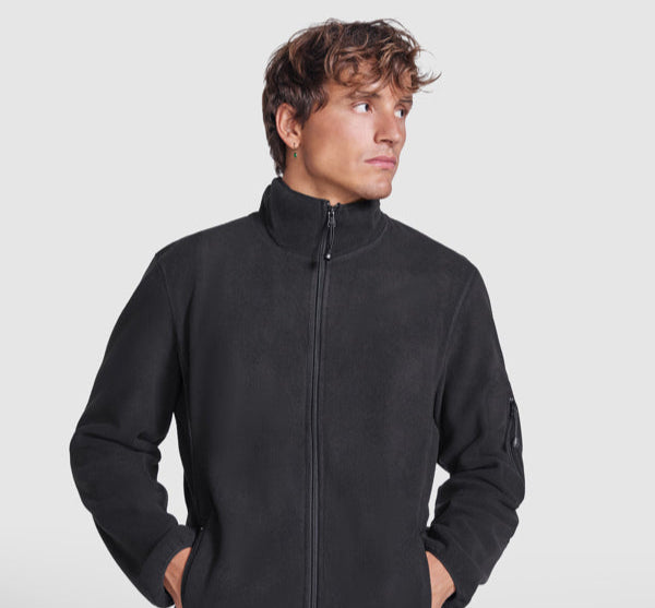 Male model wearing a black promotional fleece jacket — part of ROLY’s branded workwear and custom team clothing range.
Múnla fireann ag caitheamh seaicéad fleece dubh — cuid de raon éadaí oibre branda agus foirne ó ROLY.