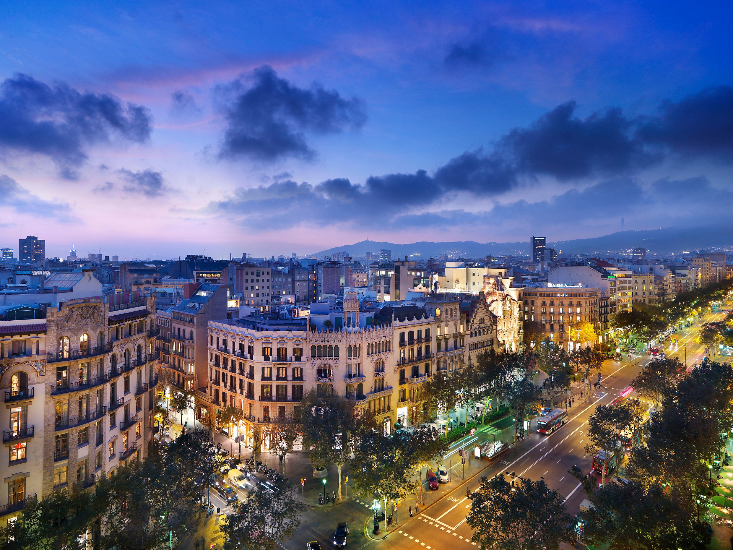 Vista panoràmica de Barcelona al capvespre, amb la ciutat il·luminada i el cel ennuvolat al fons.