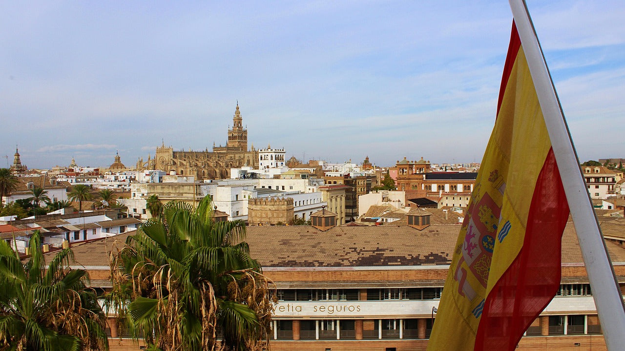 Vista de Sevilla con la bandera de España al frente, ideal para representar la distribución nacional de productos publicitarios personalizados para empresas y eventos corporativos en Andalucía.